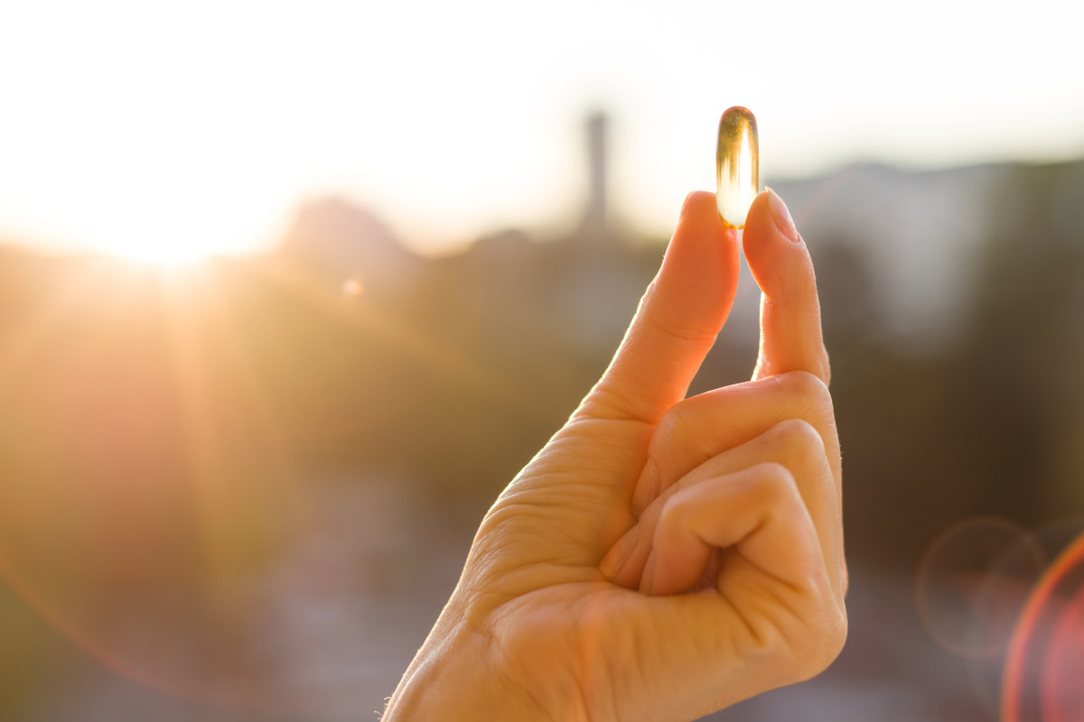 hand holding up a vitamin D pill against a sunset