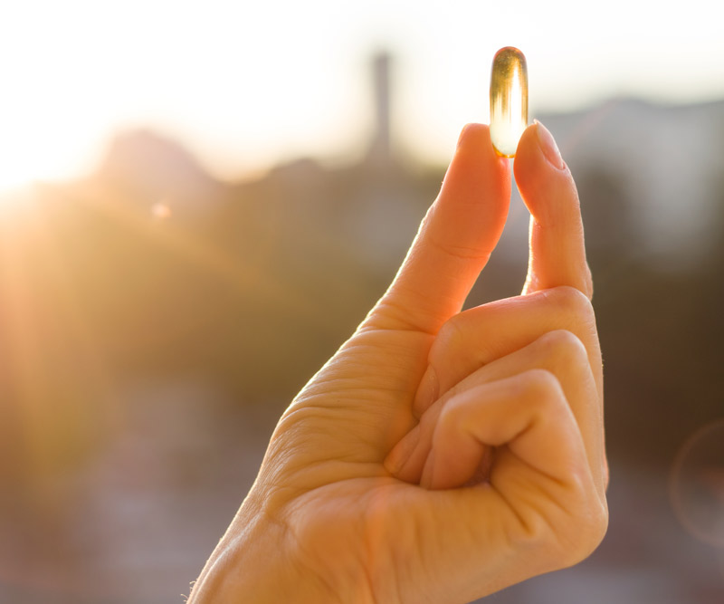 hand holding up a vitamin D pill against a sunset