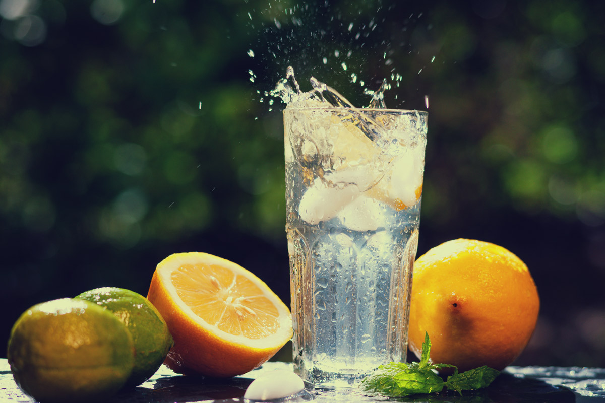 a tall glass of ice water surrounded by lemons and limes