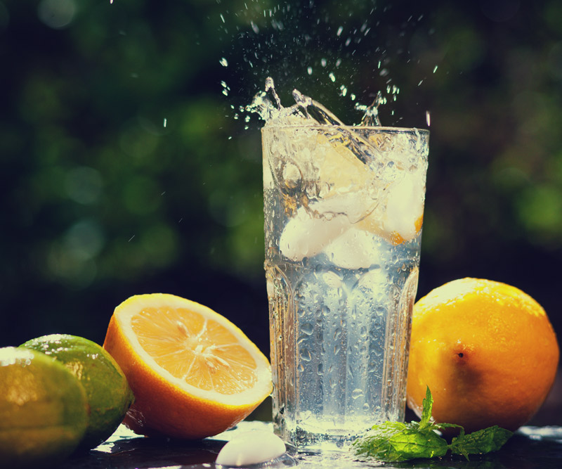 a tall glass of ice water surrounded by lemons and limes