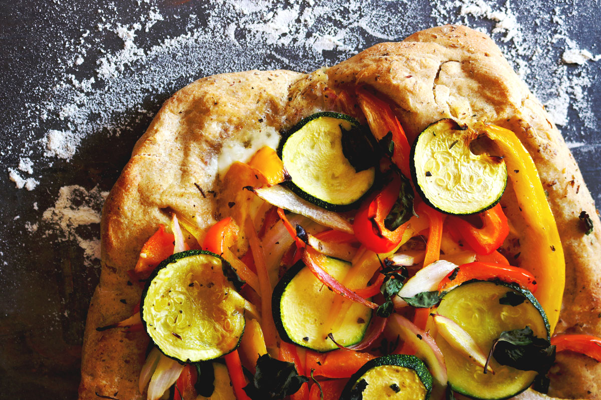 Freshly made Pizza with Peppers & Zucchini on a counter top generously dusted with flour