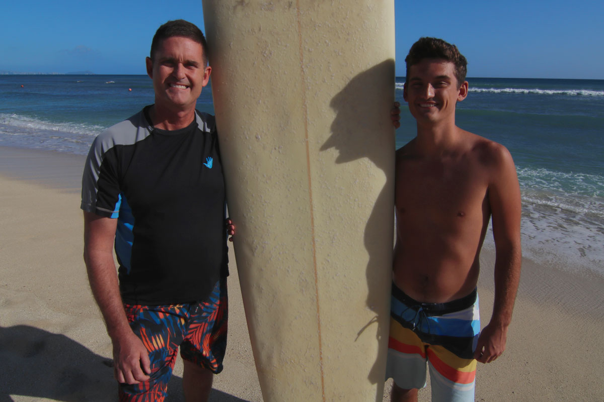 Capt. Frederick “Carl” Riedlin and his son stand with a surfboard on a beach