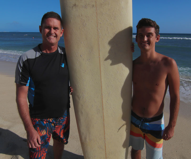 Capt. Frederick “Carl” Riedlin and his son stand with a surfboard on a beach