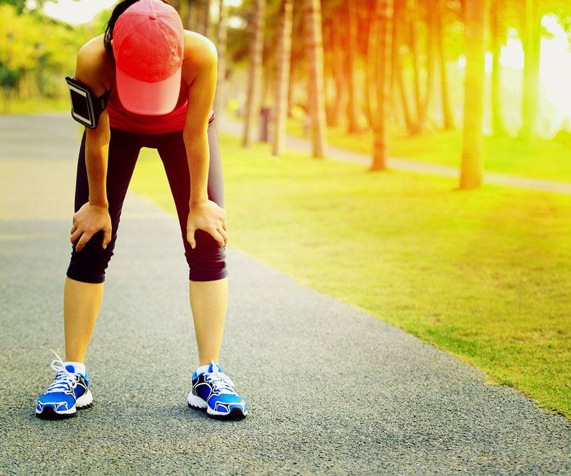 young athletic woman bent over with hands on knees as sun beats down on her back