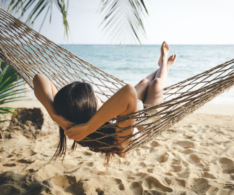 a woman relaxes in a hammock by the beach