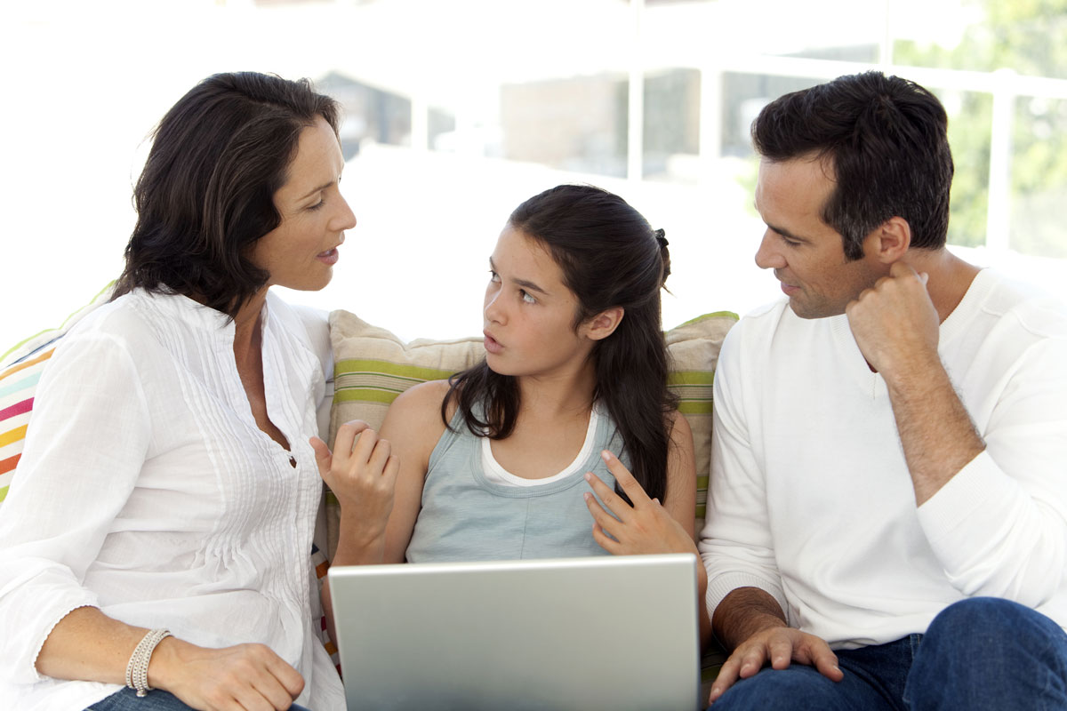 a teenage girl talks with her parents about a website on a computer