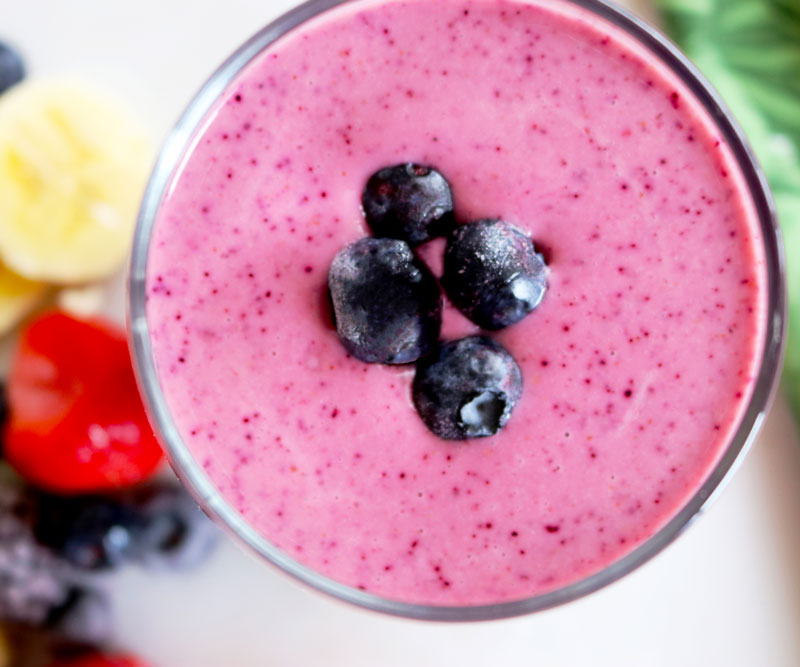 a glass of Banana Berry Blast Smoothie sits on a counter with fruit and a tropical-print napkin