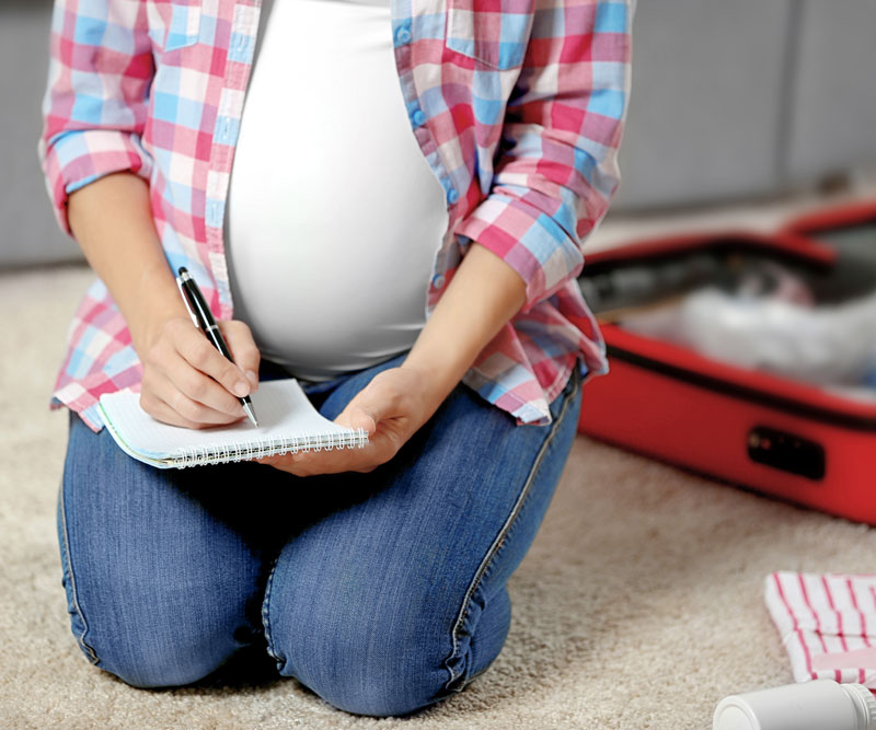 pregnant woman writing a list and packing a emergency kit