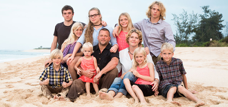 Casey Schmidt sits on a beach with her husband and nine children