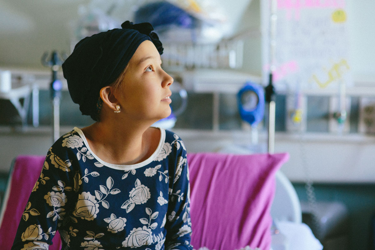 young child with cancer looks up hopefully from hospital bed