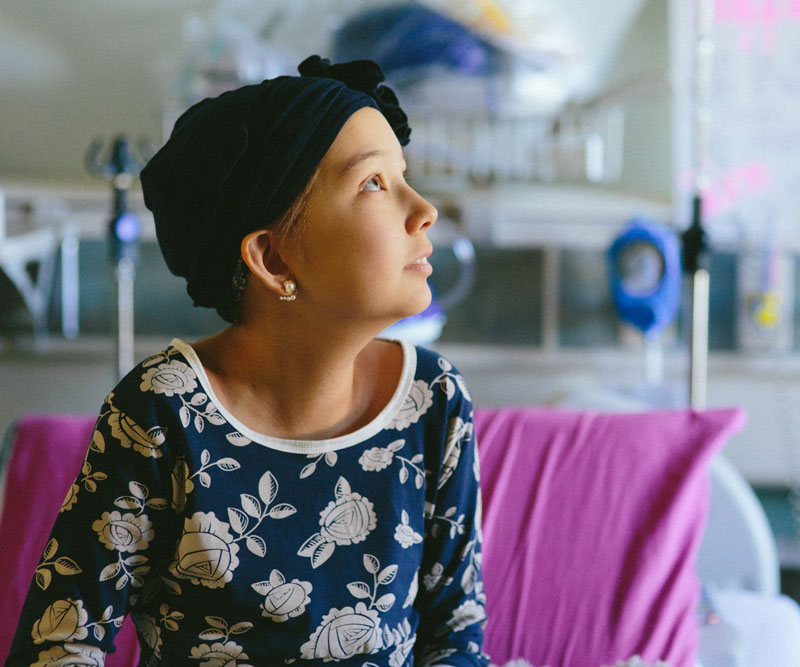 young child with cancer looks up hopefully from hospital bed