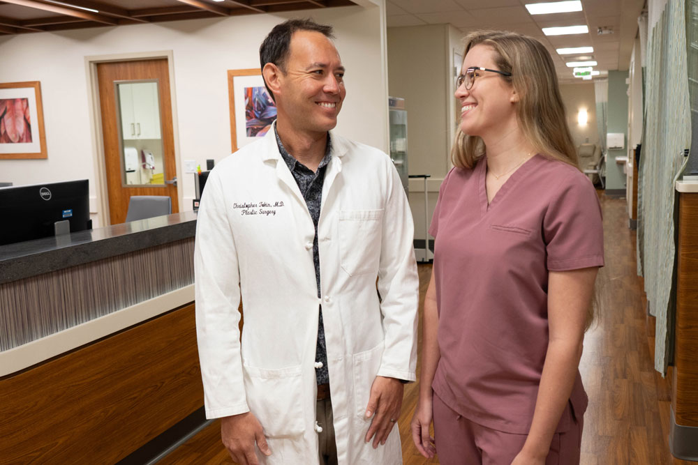 Doctor in white coat standing alongside a physician assistant in scrubs in the hallway of a medical facility. 