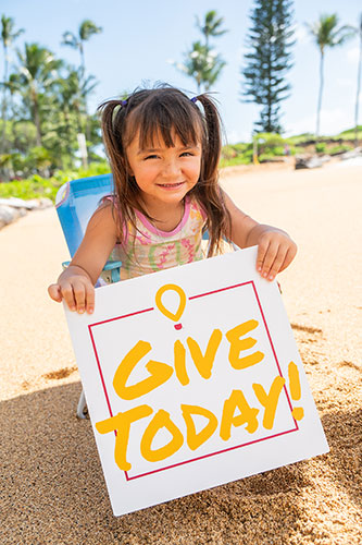 Young child in small beach chair holding sign that reads Give Today.