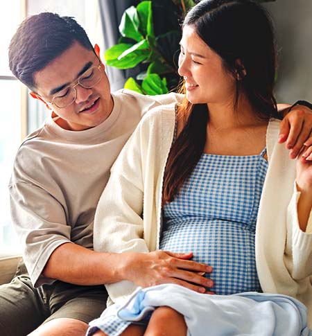 Couple sitting with man's arms around pregnant woman.  