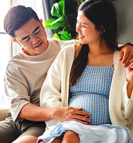 Couple sitting with man's arms around pregnant woman.  