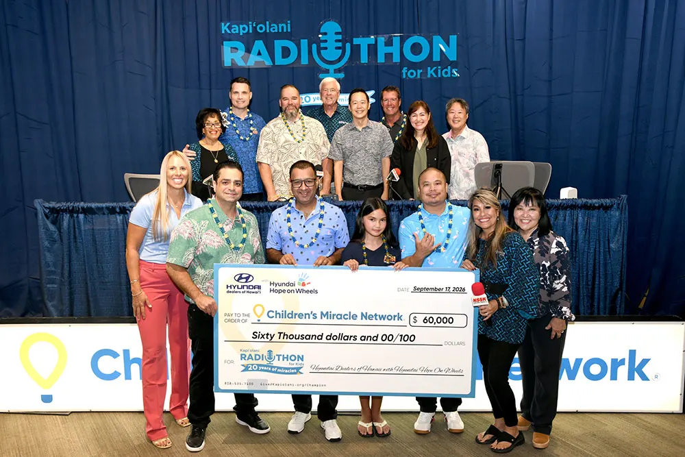 Large group shot of corporate and medical leaders with radio personalities and a giant check for $60,000.