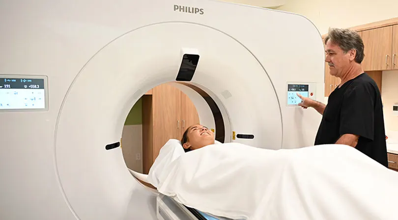 Smiling woman is about to undergo a CT scan.