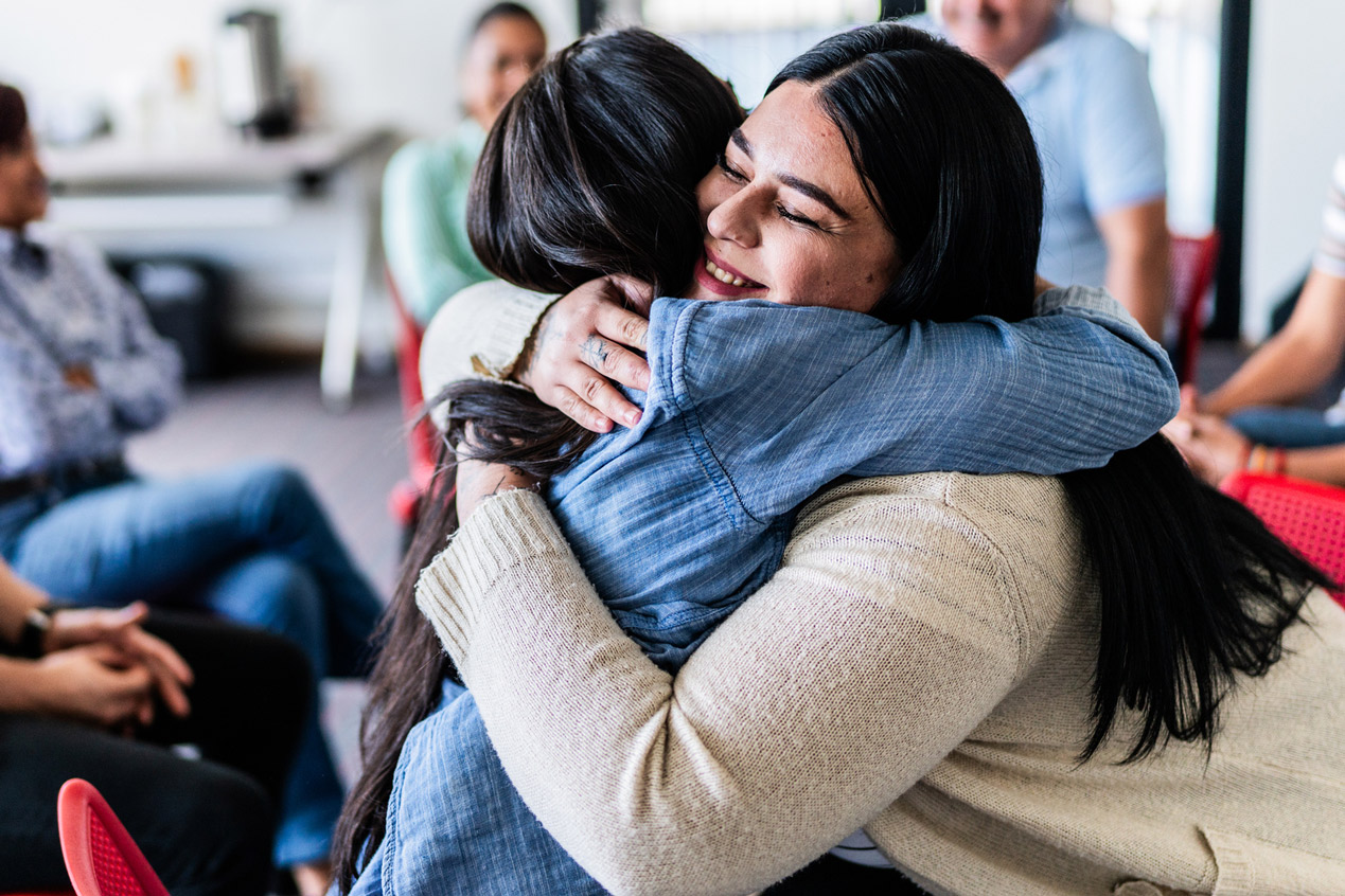 two women hug each other during a support group meeting