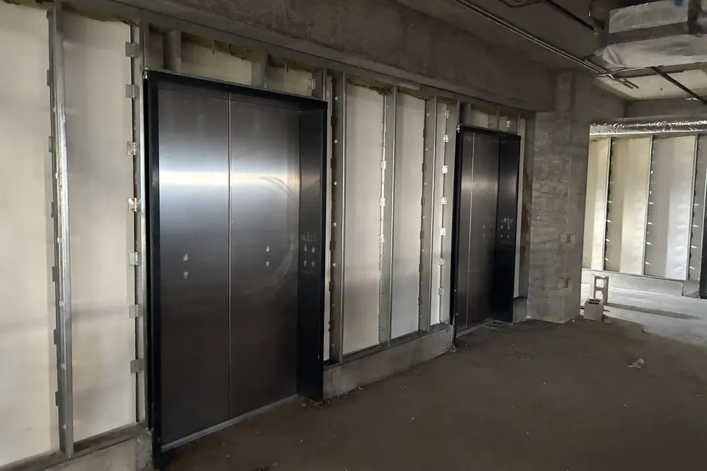 Installed elevator doors surrounded by unfinished wall framing in the lobby.