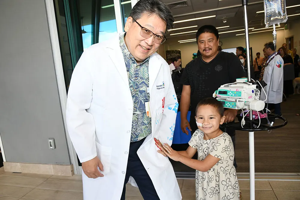 Young cancer patient with a big smile making colorful handprints on a doctor's white coat.