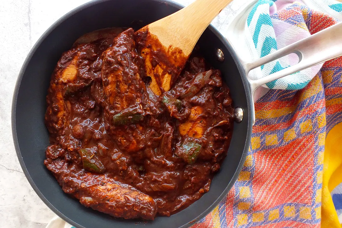 Chicken swimming in a red, brown sauce.