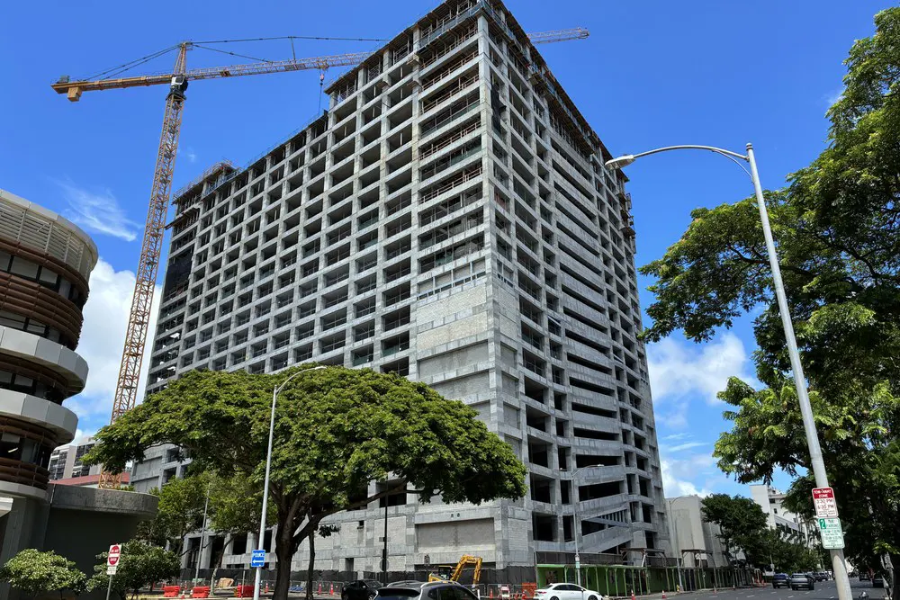 Corner street-level view of the parking building, crane, and mature trees.