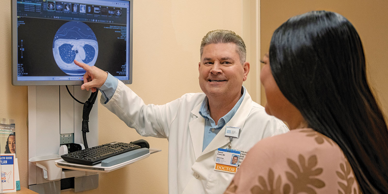 Doctor pointing at lung scan imaging while speaking with patient in exam room.