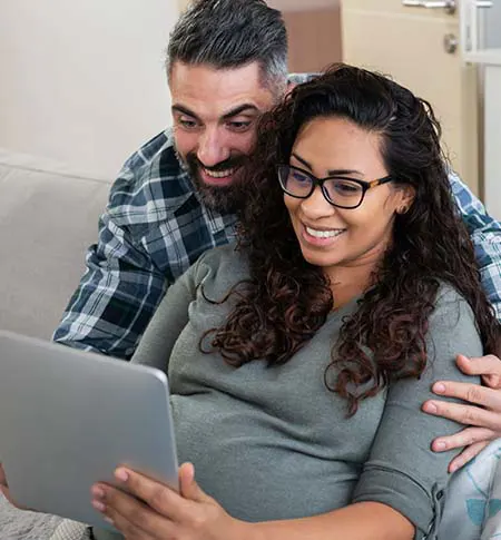 Expecting parents smiling looking at tablet.