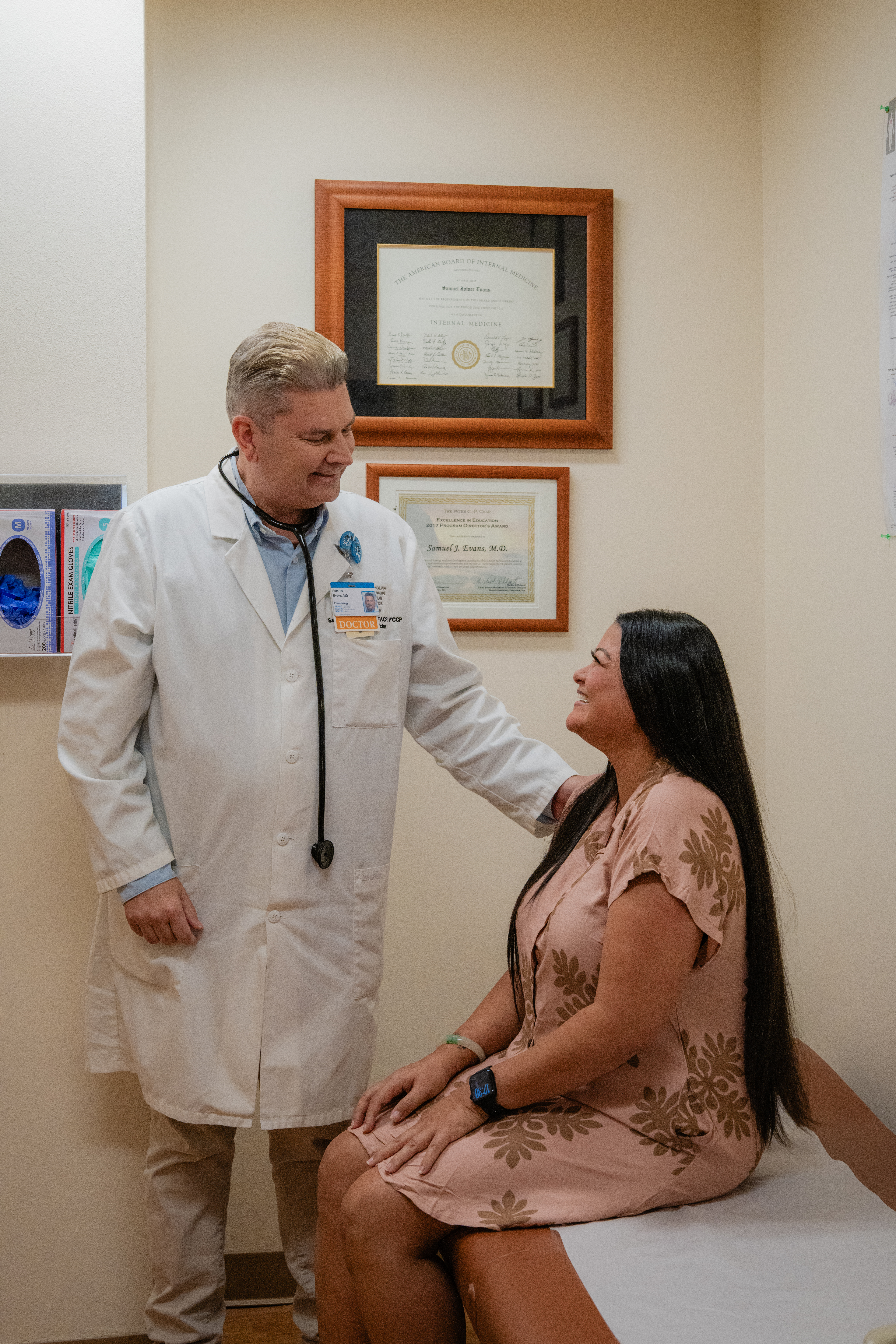 a doctor stands next to a patient who is seated in an exam room