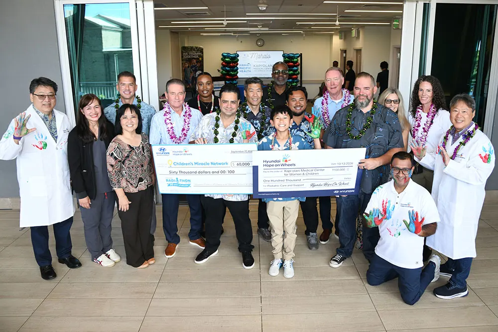 Group shot of healthcare providers, administrators, patients, and supporters holding up giant checks and painted hands.
