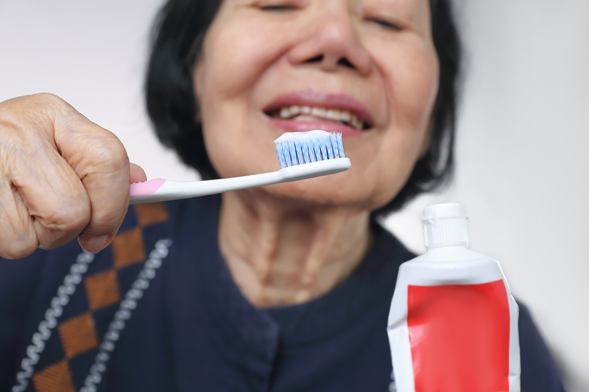 A close-up of an elderly Asian woman squeezing toothpaste onto a toothbrush.
