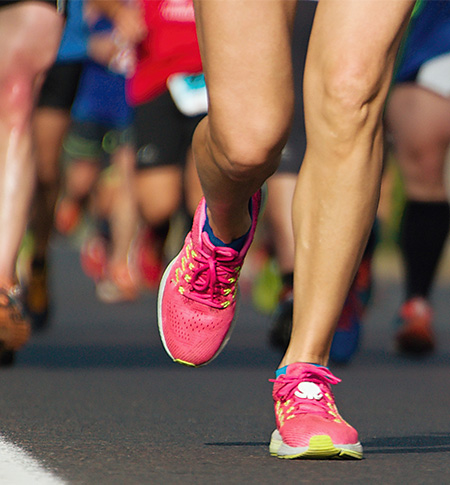 Close up view of participants running in a road race, with bright pink running shoes in the foreground.