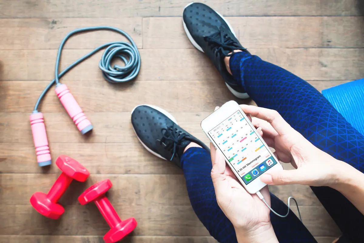 A person using phone sitting next to workout equipment.